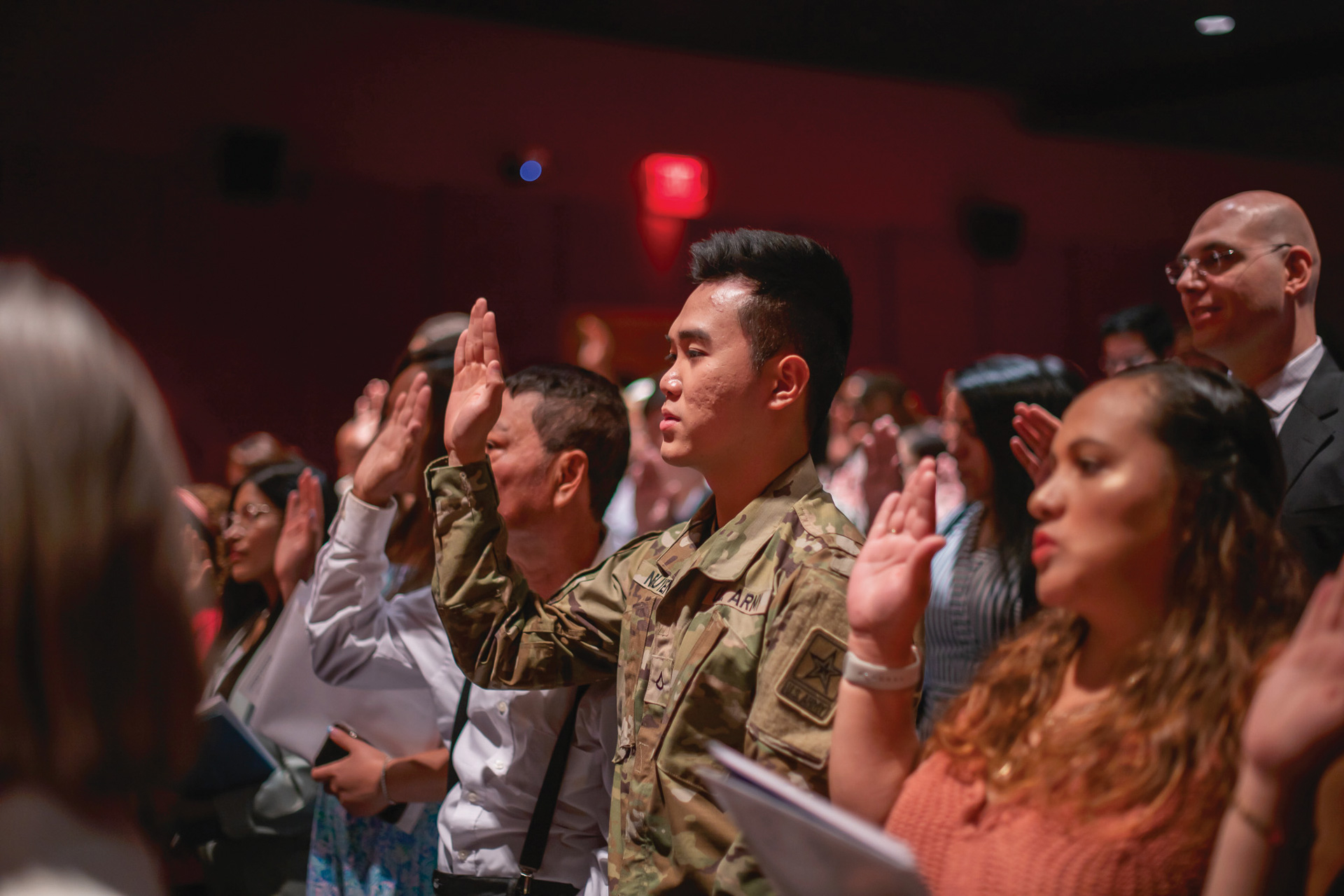 People stand in an auditorium with their right hands raised, taking the U.S. Oath of Citizenship