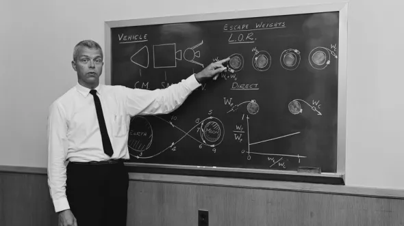 John C. Houbolt stands in front of a blackgoard with chalk darwings of the moon and physics equations