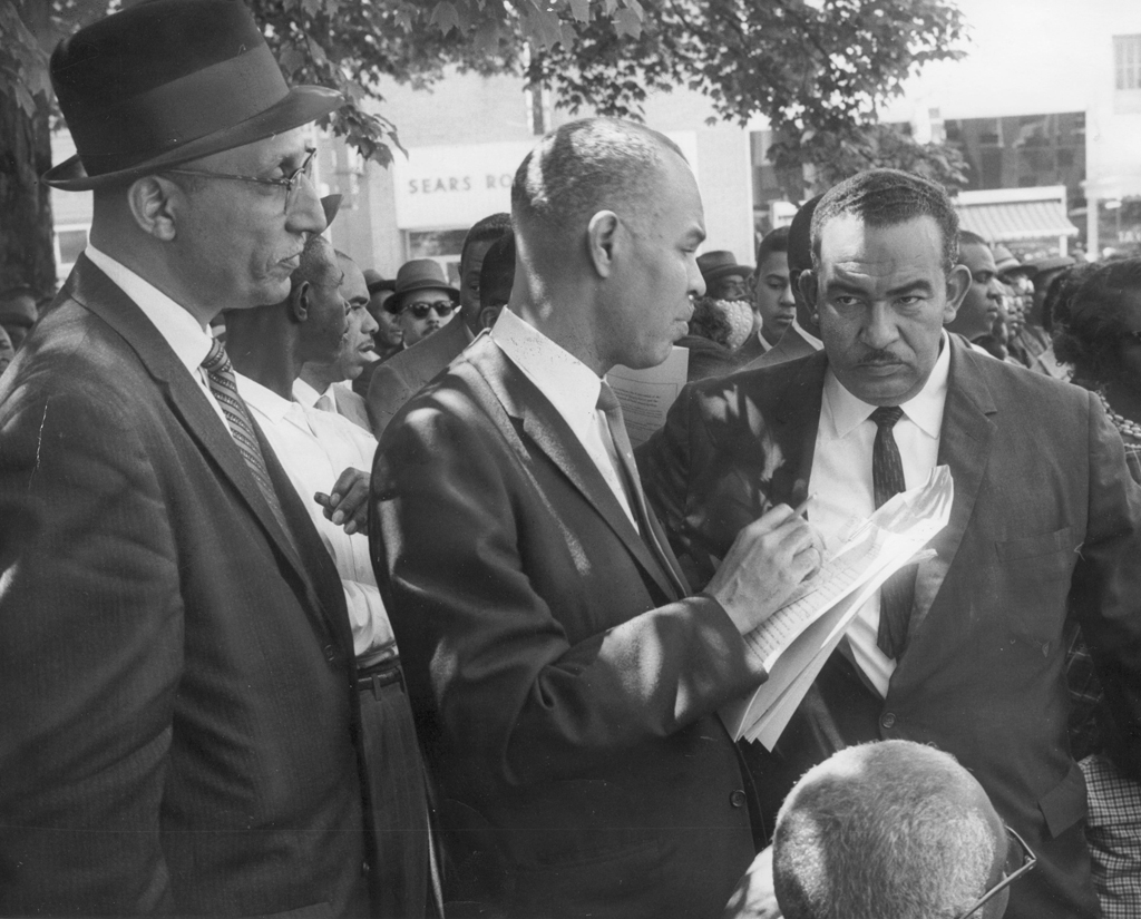 Black and white photograph of Oliver Hill, Roy Wilkins, and Reverend Francis L. Griffin speaking together at a Farmville demonstration.