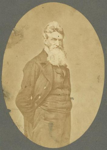 Vintage photograph of John Brown standing with his hands in his pockets, looking toward the camera.  