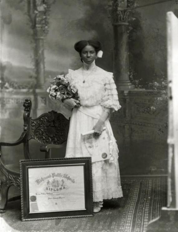 Leonie Helen Holmes, Richmond, 1911 (VHS accession number: 2003.298.29.A) Photograph of Leonie Helen Holmes, an African American graduate of Richmond Public Schools. She is standing next to a chair behind her framed diploma and wearing a white dress, holding a boquet of flowers that are tucked under her left arm. She is also holding a paper copy of her diploma in her right hand. Leonie Helen Holmes, Richmond, 1911