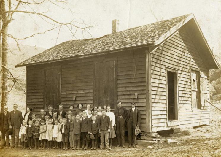 Possum Hollow Schoolhouse, Floyd County, 1910 (VHS accession number: 2001.230.308) Photograph, Possum Hollow Schoolhouse, Floyd County, taken February 25, 1910. Image of a frame school house with students and teachers posed outside. Photograph mounted on cardboard with more information about the site on the back of the card. Possum Hollow Schoolhouse, Floyd County, 1910