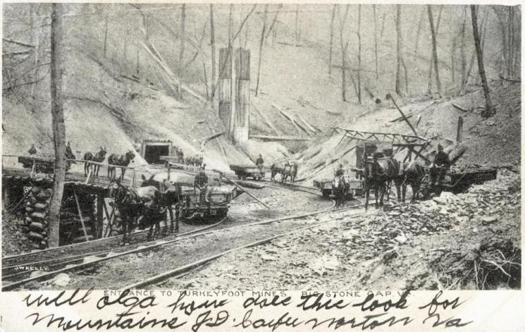 Turkeyfoot mines, Big Stone Gap, c. 1906 (VHS accession number: 2001.528.4). A black and white postcard of the entrance to Turkeyfoot mines in Big Stone Gap, Virginia. In the background is the entrance to the mine and there are track for the horsedrawn carts to be pulled on. Most of the trees are barren. There are four cars on the rails. There is writing on the obverse and reverse and a postal cancellation dated May 15, 1907 and a green one cent stamp with an image of Benjamin Franklin on it. Turkeyfoot mines, Big Stone Gap, c. 1906