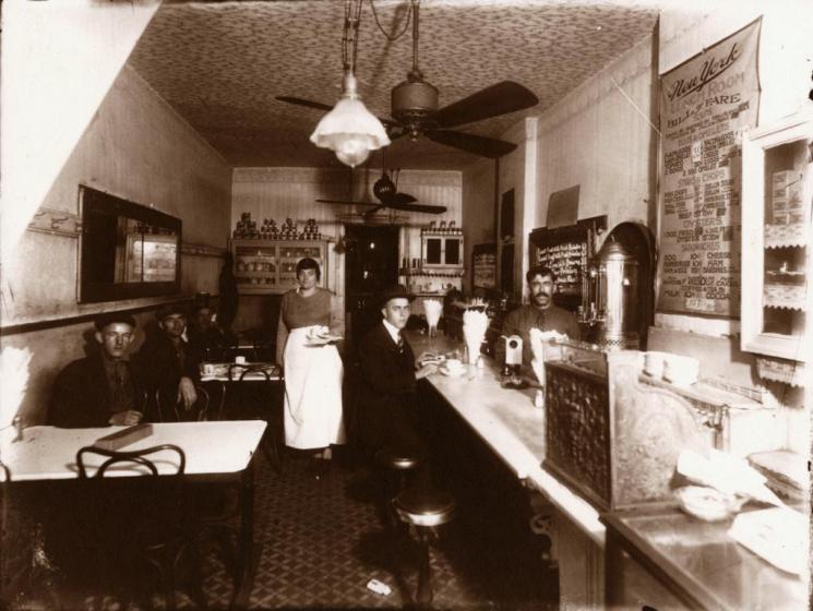 The New York Lunch Room, Norfolk, 1919 (VHS accession number: 2008.56.1). Black and white photographic print of the New York Lunch Room in Norfolk, 1919. Shows the interior of the restaurant. One man sits at the lunch counter that spans the length of the right wall. Three men are seated at the individual tables along the left wall. A waitress stands in the middle of the room and a waiter is seen behind the counter. The "Bill of Fare" is hanging on the right wall. The image is a contact print made from a glass negative, one of a set of forty-six. The negatives were rediscovered in 1968, and an edition of ten copies each was produced in 1986-87 by David E. Johnson, Peter Stewart, and Wallace E. Dreyer of Old Dominion University. The views are all of shops, mostly interiors, in downtown Norfolk, dated Nov. 1919 from calendars in some of the scenes. Project researchers were able to identify only a few of the businesses. 27.94 cm x 35.56 cm. The New York Lunch Room, Norfolk, 1919