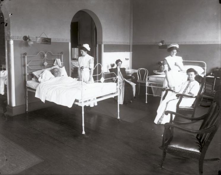 Sheltering Arms Hospital, Richmond, early 20th century (VHS accession number: 2001.230.1588.a). View of a patient room inside Sheltering Arms Hospital. There are three female patients and two female nurses shown. Sheltering Arms Hospital, Richmond, early 20th century