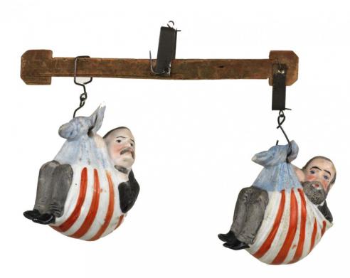 Ceramic figures of Harrison and Cleveland with each wrapped in an American flag and suspended from a wood beam