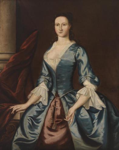 Portrait of Millicent Conway Gordon wearing a blue and red dress, facing slightly towards the left in a seated position with her left hand resting on a table. 